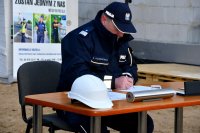 Fotografia kolorowa przedstawiająca Komendanta Wojewódzkiego Policji w Białymstoku insp.Daniela Kołnierowicza  podpisującego akt erekcyjny przy stoliku.