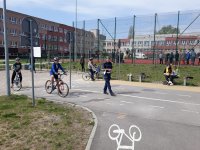 Zdjęcie kolorowe przedstawiające dwóch chłopców jadących na rowerach podczas turnieju oraz funkcjonariusza policji oceniającego jazdę.