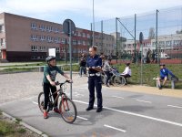 Zdjęcie kolorowe przedstawiające chłopca na rowerze oraz stojącego obok funkcjonariusza policji.