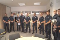 Fotografia kolorowa przedstawiająca stojących obok siebie grupę policjantów w gabinecie komendanta