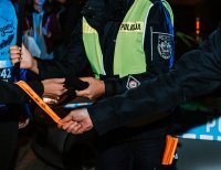Fotografia kolorowa przedstawiająca policjanta wręczającego opaskę odblaskową
