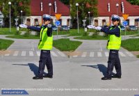 Fotografia kolorowa na której po lewej stronie policjantka kierująca ruchem prawa rękę ma wyciągniętą przed siebie z kolei lewą w bok