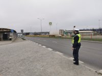 Fotografia przedstawiająca policjanta stojącego na drodze z uniesioną tarczą do zatrzymywania samochodów.