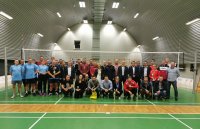 Fotografia kolorowa przedstawiająca stojących  wszystkich uczestników turnieju piłki siatkowej..