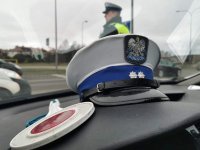 Fotografia kolorowa przedstawiająca lizak policyjny oraz czapkę leżąca na kokpice w samochodzie.