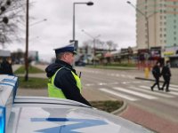 Fotografia kolorowa przedstawiająca policjanta tyłem kontrolującego uczestników ruchu drogowego.