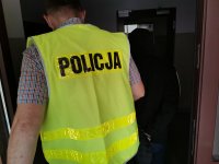 policjanci w żółtych kamizelkach z napisem policja z zatrzymanym mężczyzną w kajdankach