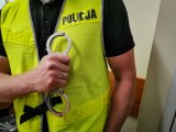 zdjęcie policjanta w żółtej kamizelce, który trzyma kajdanki