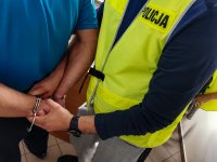 policjant ubrany w żółtą kamizelkę, zakładający zatrzymanemu kajdanki na ręce