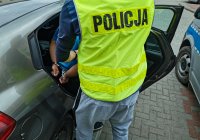 policjant w żółtej kamizelce, który umieszcza zatrzymanego w samochodzie