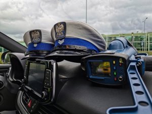policyjne czapki policjantów z Ruchu Drogowego leżące na kokpicie radiowozu. Obok urządzenie do pomiaru prędkości
