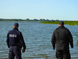 policjant i funkcjonariusz straży rybackiej stojący nad brzegiem rzeki