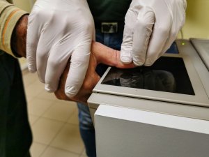 policyjny technik kryminalistyki pobiera na urządzeniu odcisk palca od osoby zatrzymanej