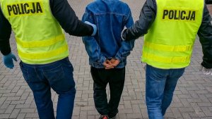 policjanci kryminalni prowadzą zatrzymanego mężczyznę, który ma założone kajdanki na rękach