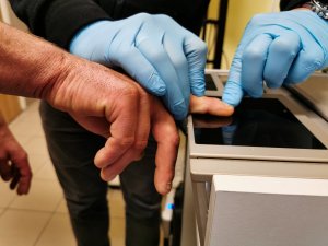 technik kryminalistyki pobiera odciski palców od osoby zatrzymanej