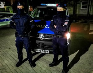 Policjanci z Wydziału Patrolowo-Interwencyjnego Komendy Miejskiej Policji w Białymstoku, umundurowani, stoją przed radiowozem policyjnym