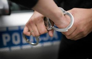 policjant zakłada kajdanki na ręce osoby zatrzymanej