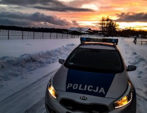 policyjny radiowóz z włączonymi światłami, który stoi na zaśnieżonej drodze