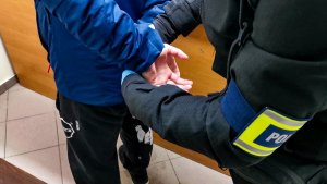 policjant ubrany w cywilne ubrania, zakłada zatrzymanemu kajdanki na ręce trzymane z tyłu