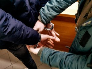 policjant w ubraniach cywilnych zakłada mężczyźnie kajdanki na ręce trzymane z tyłu