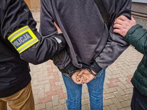 policjanci trzymający zatrzymanego mężczyznę, który ma założone kajdanki na ręce trzymane z tyłu