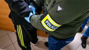 policjant w ubraniach cywilnych zakłada zatrzymanemu mężczyźnie kajdanki na ręce trzymane z tyłu