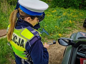 Policjantka stojąca przy kontrolowanym samochodzie w ręku ma urządzenie do badania alkomatem