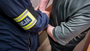 policjant kryminalny w cywilnych ubraniach zakłada zatrzymanemu 71-latkowi kajdanki na ręce trzymane z tyłu