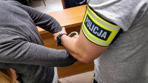 policjant w cywilnych ubraniach zakłada kajdanki na ręce trzymane z tyłu