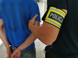 policjant z opaską na ręku z napisem policja trzyma za ramię zatrzymanego