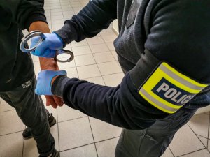 policjant kryminalny w cywilnych ubraniach zakłada zatrzymanemu kajdanki na ręce trzymane z tyłu