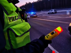 Policjant trzymający urządzenie do badania trzeźwości ze świecącą się czerwoną lampką.
