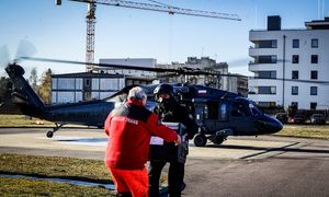 Policjant przekazujący ratownikowi walizkę z narządem, w tle helikopter