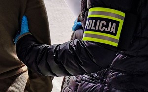 Policjanta z opaską z napisem policja, doprowadzający zatrzymanego