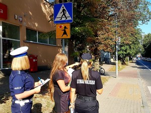 Policjantka ze strażniczką miejską i urzędniczką sprawdzają oznakowanie przy szkołach.