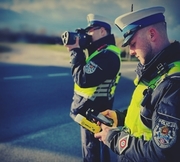 dwóch policjantów, jeden z nich trzyma przy twarzy urządzenie do mierzenia prędkości