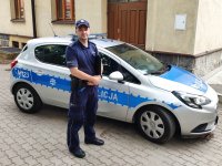 Zdjęcie w kolorze. Na pierwszym planie dzielnicowy, który odnalazł zaginionego 84-latka. W tle radiowóz.