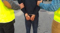 Fotografia kolorowa przedstawiająca zatrzymanego w kajdankach z rękami trzymanymi z tyłu
