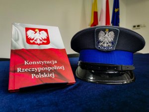 na niebieskim materiale ustawiona po lewej Konstytucja Rzeczpospolitej Polskiej z Orłem, a po prawej galowa policyjna czapka posterunkowegho