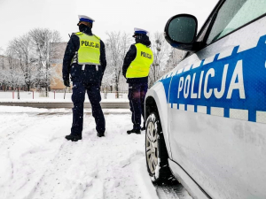 policjanci obserwujący ruch drogowy, stojący przy jezdni przed radiowozem, w tle aura zimowa