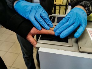 technik kryminalistyki, który pobiera odciski palców od zatrzymanej osoby