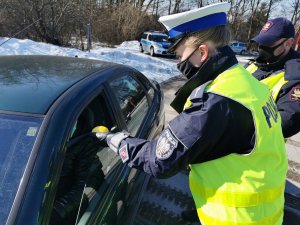 Policjantka wręczająca cytrynę kierowcy, w tle tuż za nią funkcjonariusz Straży Ochrony Kolei