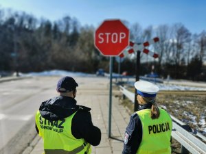 Policjantka i i funkcjonariusz Straży Ochrony Kolei stojący przed przejazdem kolejowym