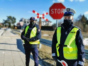 Po prawej stronie fotografii policjantka po lewej Strażnik Ochrony Kolei stojący przodem w tle przejazd kolejowy i znak stop
