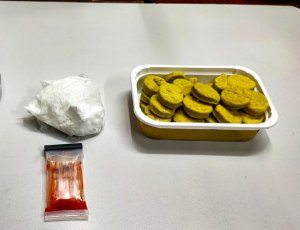 po lewej stronie biały proszek-amfetamina, po prawej stronie w pudełku żółte ciasteczka z marihuaną. Poniżej narkotester, który zabarwił się na czerwono