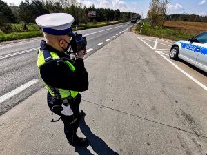 policjant w trakcie czynności pomiaru prędkości; w tle droga