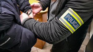 policjant zakłada kajdanki mężczyźnie na ręce trzymane z tyłu