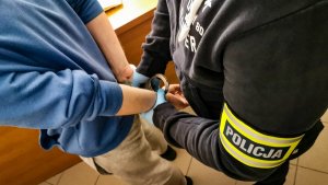 policjant kryminalny w cywilnych ubraniach zakłada kajdanki na ręce trzymane z tyłu