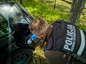policyjny technik kryminalistyki podczas robienia oględzin pojazdu Policjant zbiera pędzelkiem odciski palców