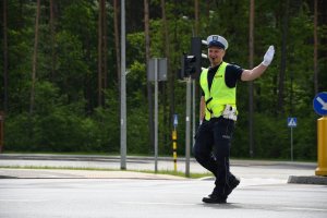 policjant z Wydziału Ruchu Drogowego podczas kierowania ruchem drogowym. Policjant ma założone białe rękawiczki